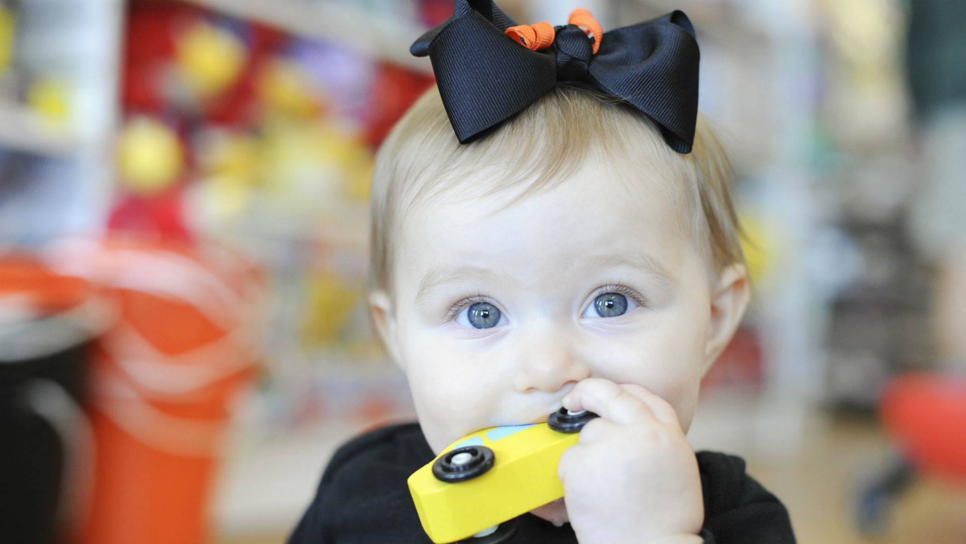 baby girl with car in mouth and black bow